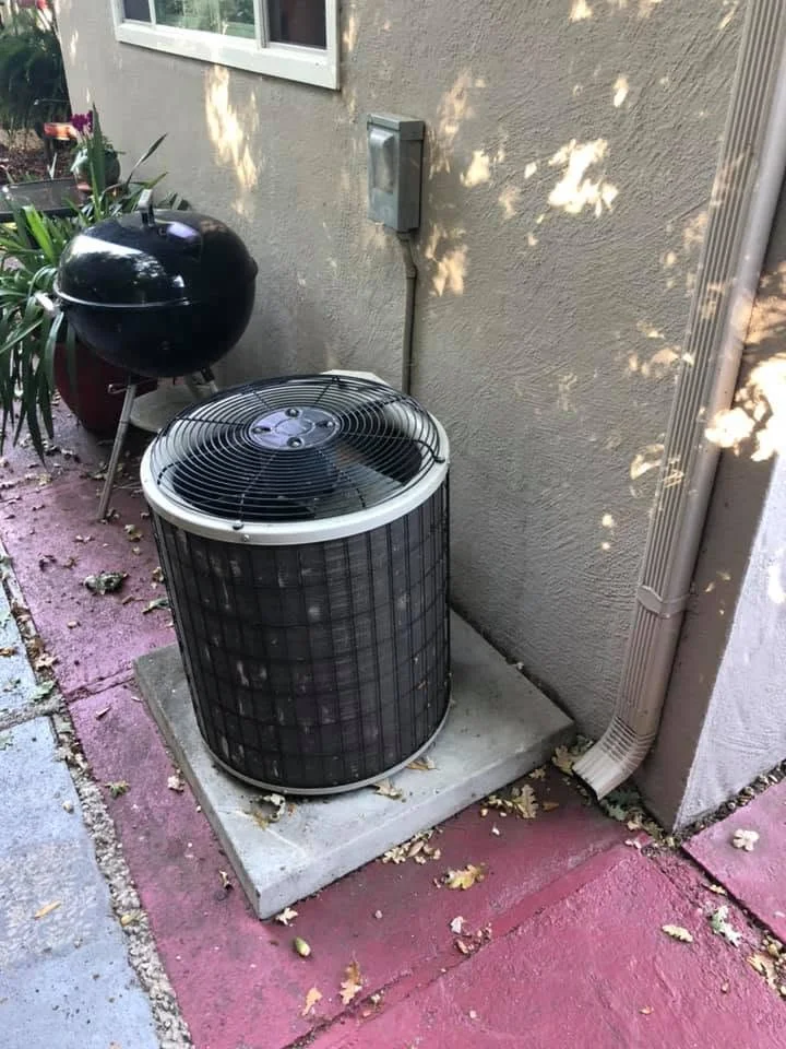 Black cylindrical AC condenser unit installed on concrete pad against stucco exterior wall