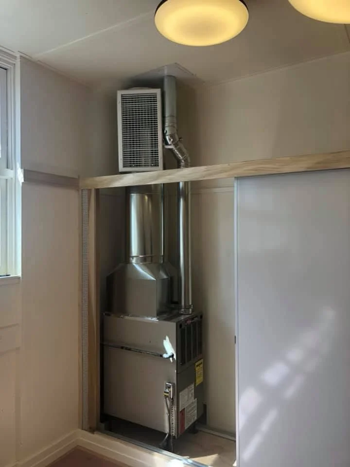 High-efficiency furnace with air handler, metal ductwork, and wooden frame enclosure in finished interior space