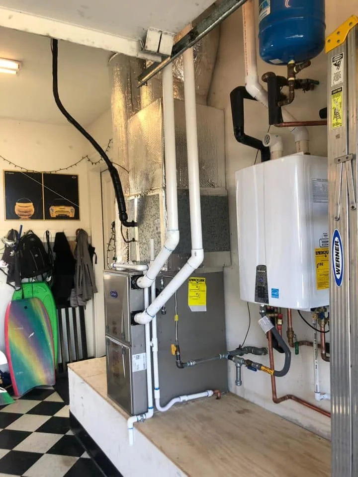 Tankless water heater with white PVC piping, expansion tank, and HVAC system components in garage