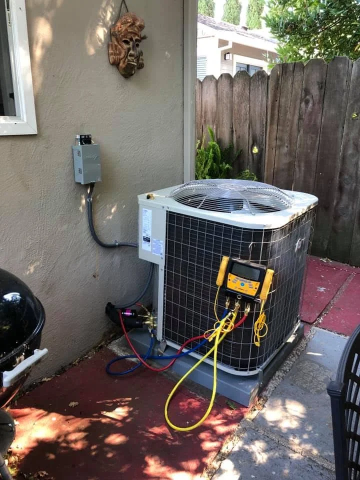 AC condenser unit installation with yellow service hoses and electrical disconnect on stucco wall