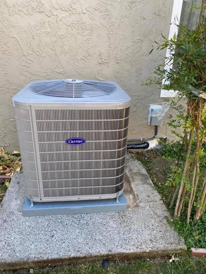 Carrier AC condenser unit installed on concrete pad with refrigerant lines and electrical connections