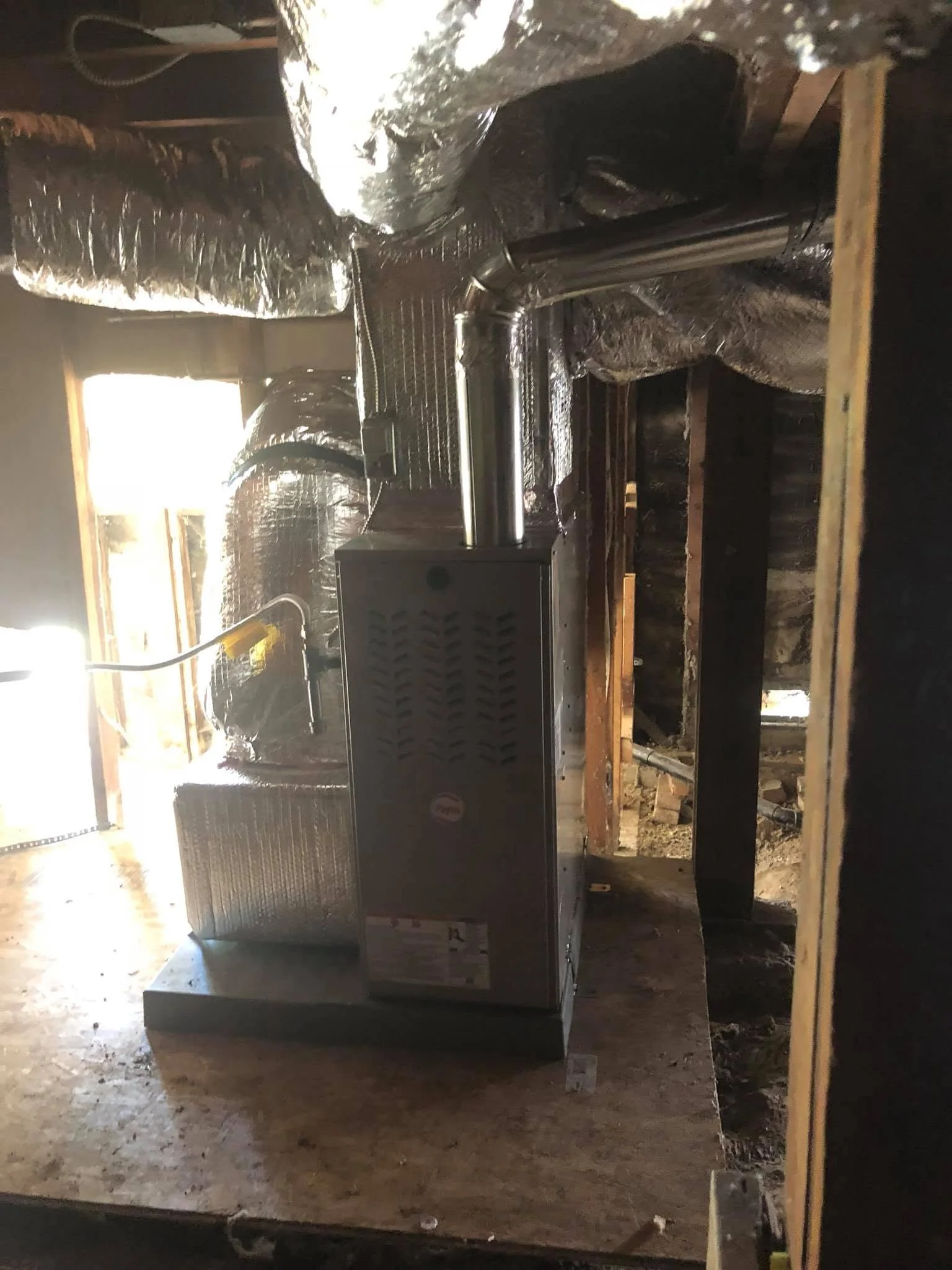Black furnace unit with insulated ductwork and reflective wrap in basement installation