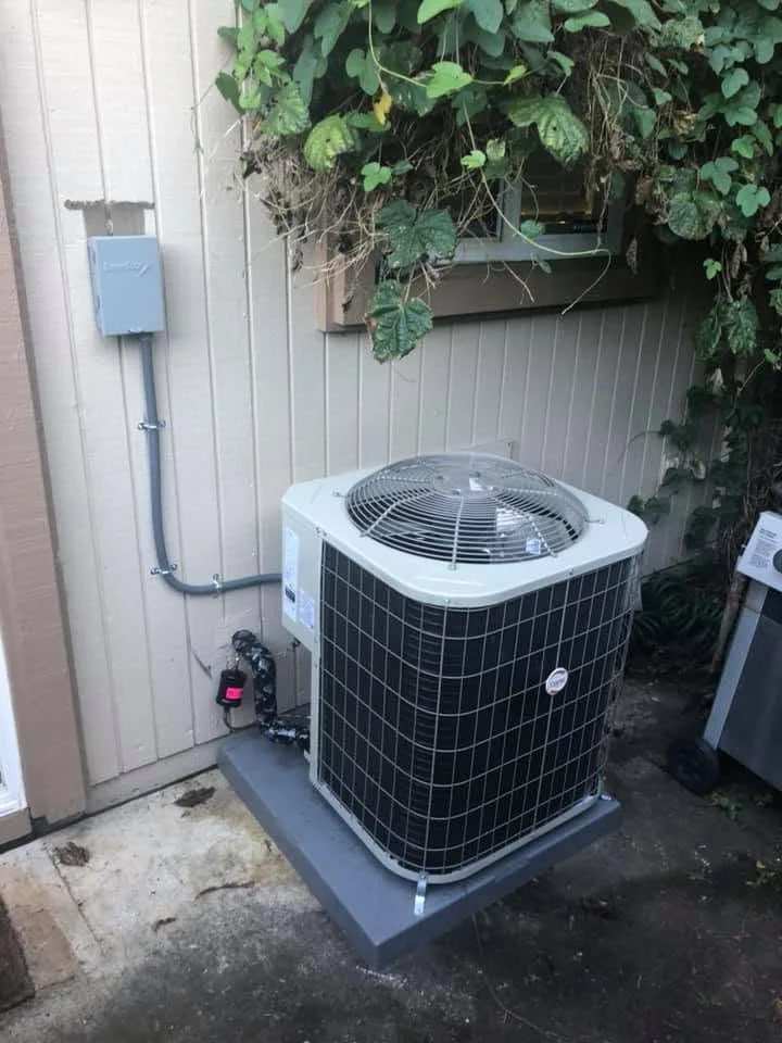 New AC condenser unit on concrete pad with refrigerant lines and disconnect switch